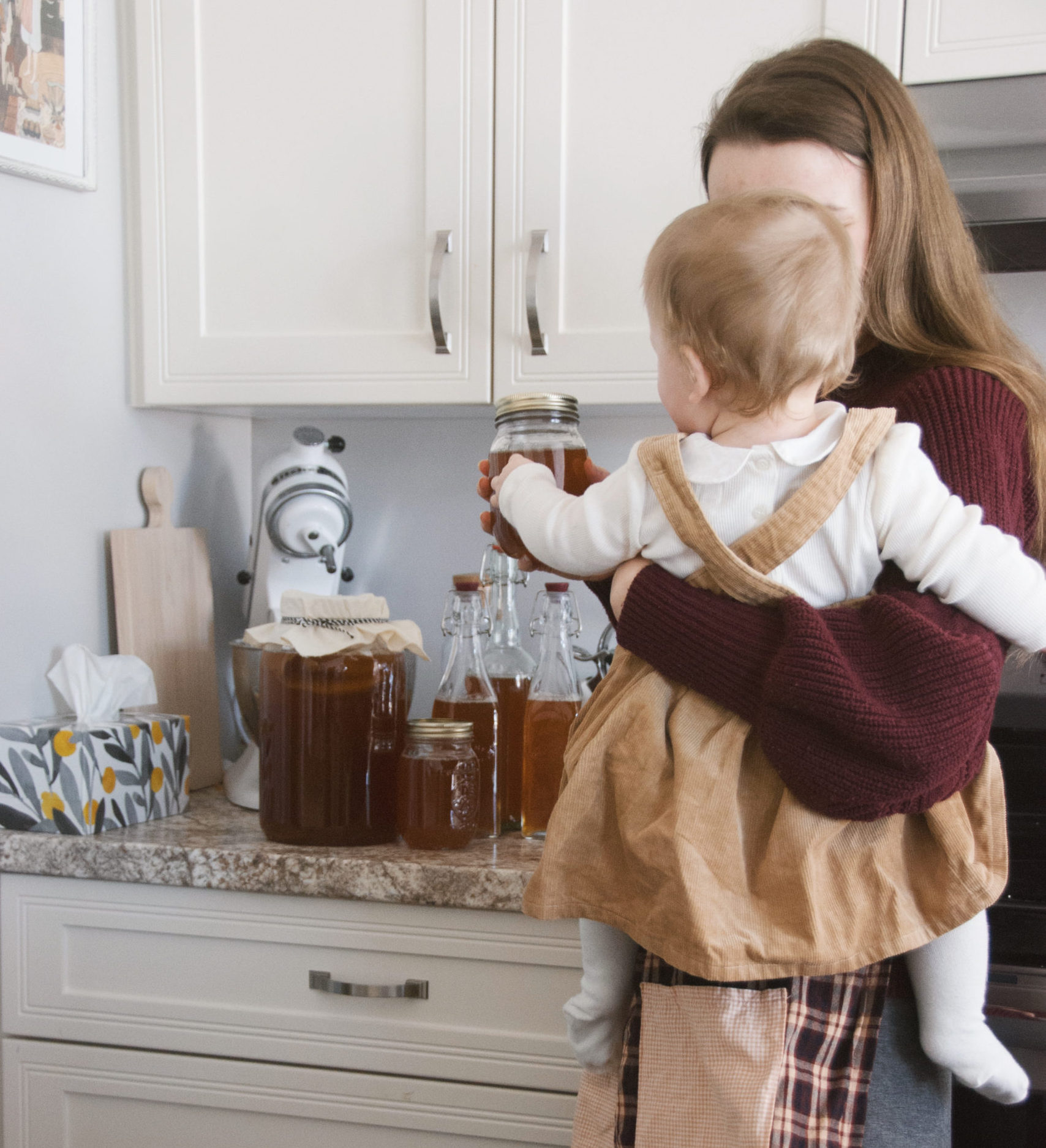 A mother holding her daughter and showing her the kombucha she just made